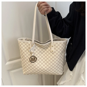 Detailed close-up of beige tote bag featuring M-letter print and golden metal charm