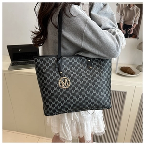 Detail of large tote bag with M-letter pattern and golden logo pendant on the strap