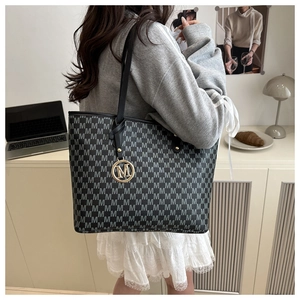 Detail of large tote bag with M-letter print, black leather handles and gold charm