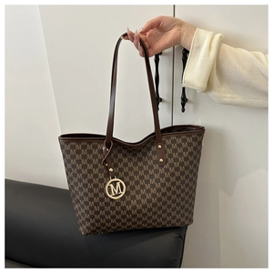 Detailed macro of coffee patterned tote bag featuring a golden M letter metal pendant