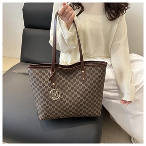 Detail of monogram tote bag with gold M-logo pendant and durable brown leather handles