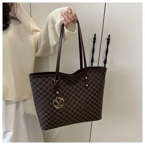 Close-up of brown tote bag with M-letter pattern and golden metal logo pendant