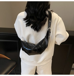 Detail of a black glossy croissant bag with crescent shape and silver metal buckle strap