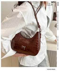Braune Crescent-Tasche mit Krokoprägung und silberner Metallschleife als Schultertasche