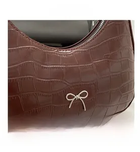Makro-Detail der dunkelbraunen Krokodil-Textur und Silber-Schleife auf der Tasche