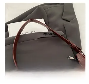 Detailansicht braune Schultertasche mit Kroko-Prägung auf grauem Anzug-Hintergrund