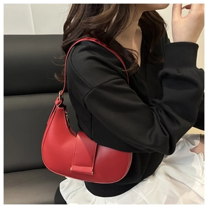 Close-up of red hobo bag with top zipper and wide buckle strap on a black sofa