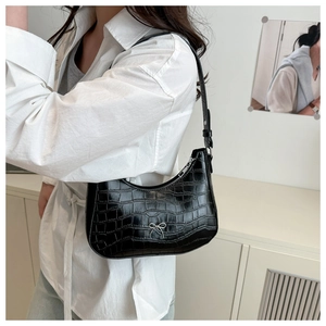 Nahaufnahme der schwarzen Tasche mit Krokostruktur, Silberschleife und Outfit-Detail