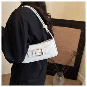 Close-up of white leather baguette bag with large gold buckle and knotted shoulder strap