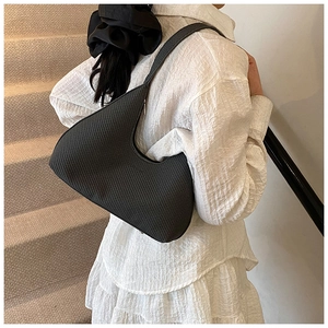 Detail of black crescent shoulder bag with woven texture worn on shoulder by a model