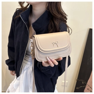 Detail of a chic beige crossbody bag with a slim golden bow buckle and fine PU texture
