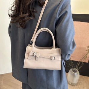 Chic beige crossbody bag with bow detail shown on a model in a modern interior setting