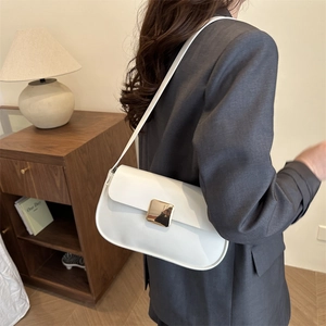 Minimalist white leather underarm bag with gold metal buckle shown on shoulder in home setting