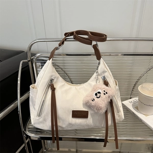 Chic cream tote bag with brown leather accents and silver zippers on a metal rack