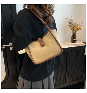 Detail of minimalist beige shoulder bag with brown trim and snap button closure