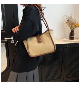 Close-up of beige tote bag with brown trim and magnetic flap clasp worn by a model