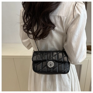 Detail view of black quilted crossbody bag with silver buckle worn by a model