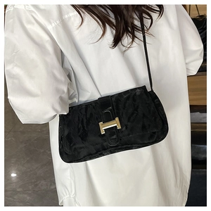 Detail of black velvet baguette bag with golden H-buckle on a white shirt model