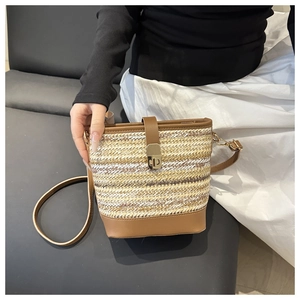 Detail of straw woven bucket bag with brown leather trim and golden twist lock closure