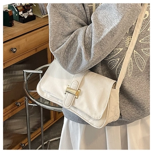 Detail shot of white leather baguette bag featuring a gold metal clasp and accordion side pleats