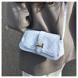 Detail of light blue patent leather baguette bag with golden H buckle on a gray suit