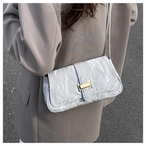 Close-up of silver pleated faux leather texture and gold H-shaped clasp on a baguette bag