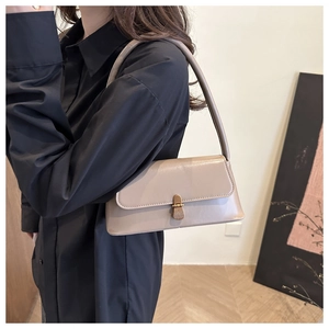 Detailed side view of minimalist beige baguette bag worn on shoulder over light-colored coat