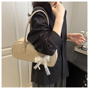 Detail of beige leather Boston bag with lace bow and pearl chain on a black shirt