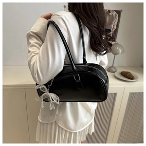 Detail of black glossy Boston bag with pearl lace bow pendant shown on model's shoulder
