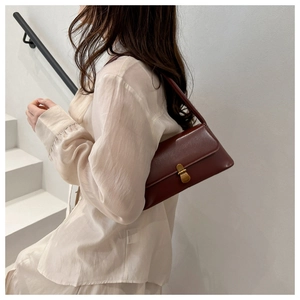 Detail of vintage baguette bag with glossy leather texture and gold buckle on model