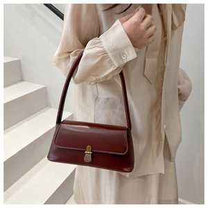 Detail of wine red minimalist leather shoulder bag with brass buckle on model