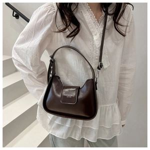 Detail view of a dark brown glossy leather saddle bag worn by a model as a crossbody bag
