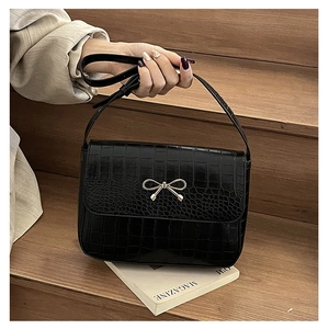 Détail d'un sac en cuir noir motif crocodile avec un fermoir papillon doré chic