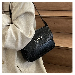 Détail du sac noir texture crocodile avec boucle nœud argenté sur blazer beige