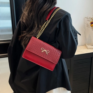 Sac à bandoulière rouge élégant avec nœud doré et chaîne porté par un mannequin