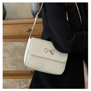 Detail of white crocodile pattern shoulder bag with golden bow metallic decoration