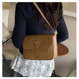 Détail du sac à bandoulière marron motif crocodile avec boucle dorée sur robe en dentelle