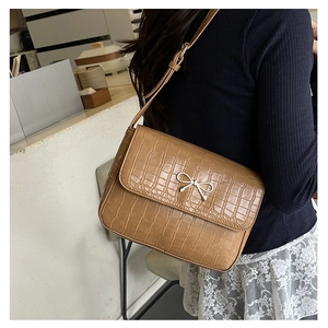 Close-up of brown crocodile texture leather bag with silver bow ornament buckle