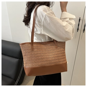 Side view of large straw tote bag with brown leather handles and base worn by a model