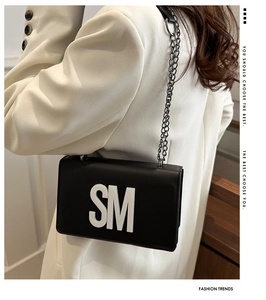 Detail shot of a black leather crossbody bag with a white SM letter and chain strap