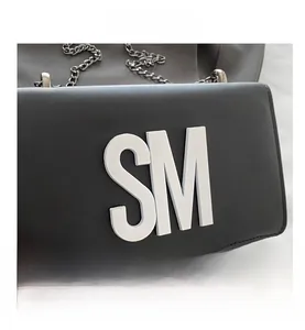 Close-up of black leather crossbody bag featuring a large white SM logo and metal chain strap