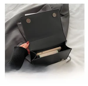 Detail show of black faux leather crossbody bag with dual magnetic closures and chain strap