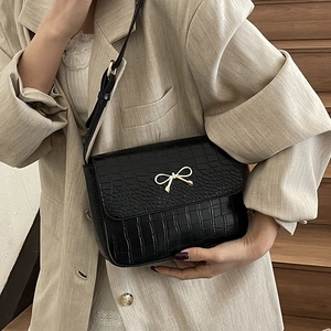 Sac à bandoulière noir motif crocodile élégant avec boucle nœud doré sur mannequin