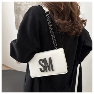 Close-up of white crossbody bag with black SM logo and fine metal chain strap