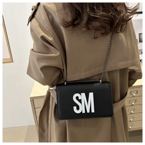 Detail of black crossbody bag with white SM letters and a dark metal chain strap