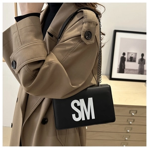 Detail of black crossbody chain bag with bold white SM lettering on matte leather