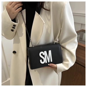 Detail of black leather crossbody bag with white SM lettering and metal chain strap