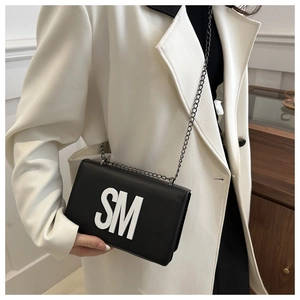 Detail of a chic black square crossbody bag with white SM letters and chain strap