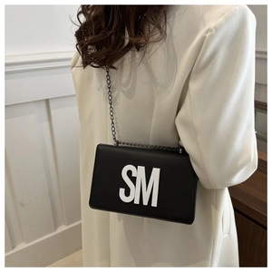 Detail of a chic black square bag with white SM letters and a metal chain strap