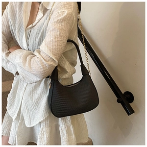 Detail of black textured hobo bag with gold chain strap on model's shoulder